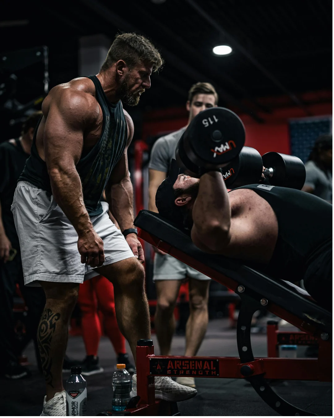 An athlete lifting dumbbells while a coach watches closely