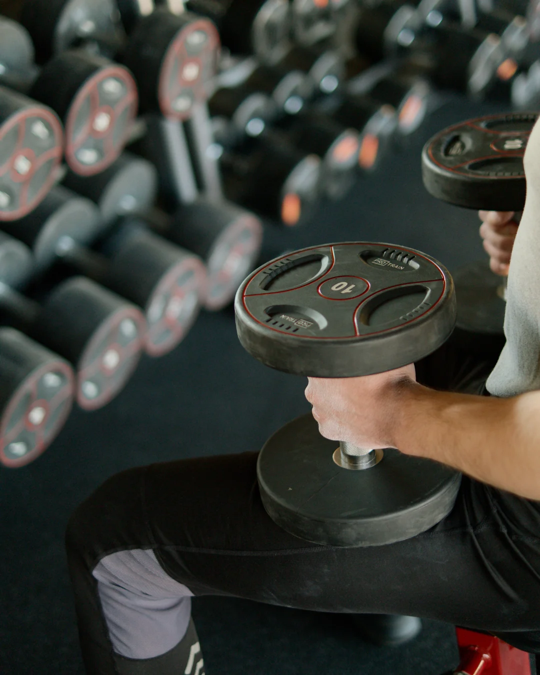 An athlete selecting dumbbells beside a weight rack